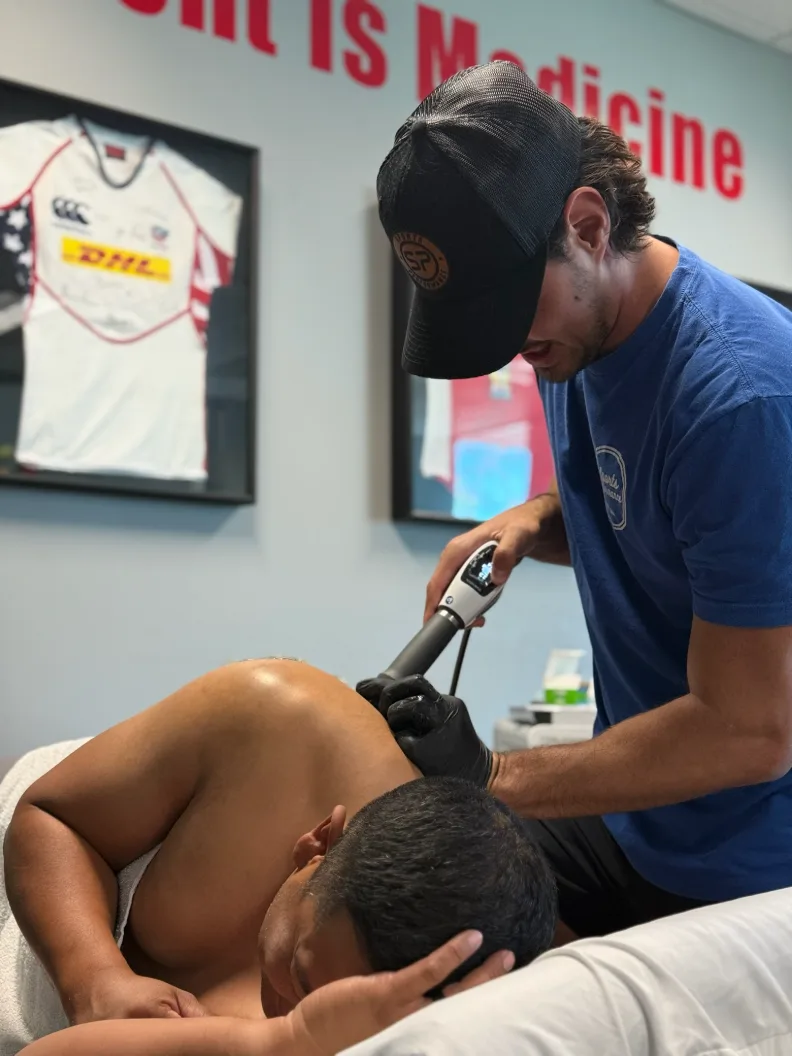 A Sports Performance clinician applying shockwave therapy to a client's upper back